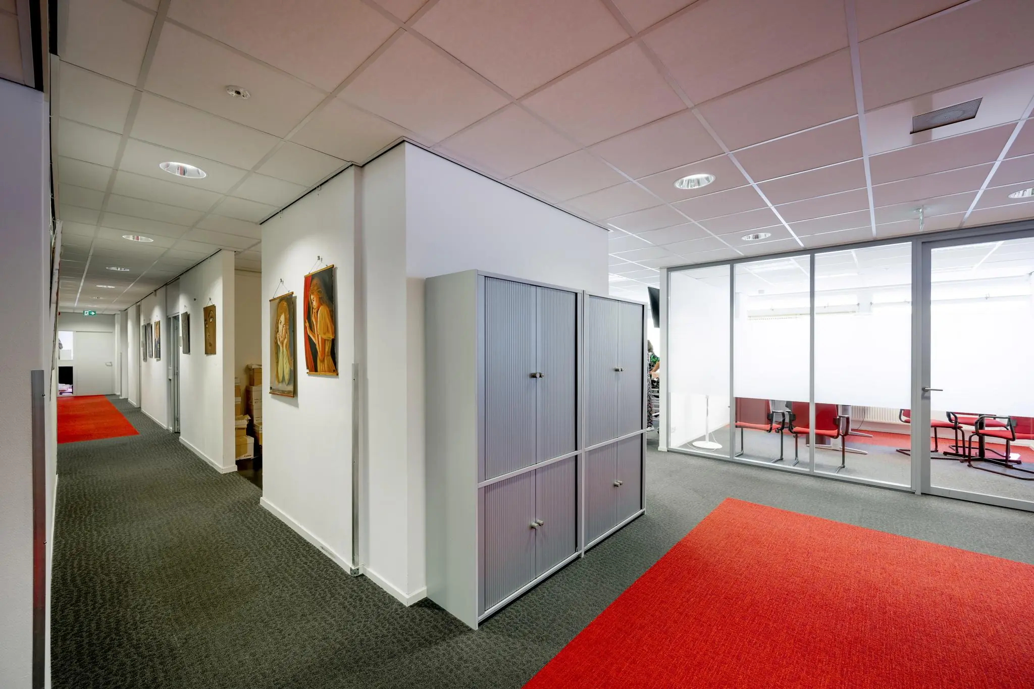 Modern kantoorinterieur aan de Jan Tooropstraat met rood tapijt, glazen vergaderruimte en schilderijen aan de muur.